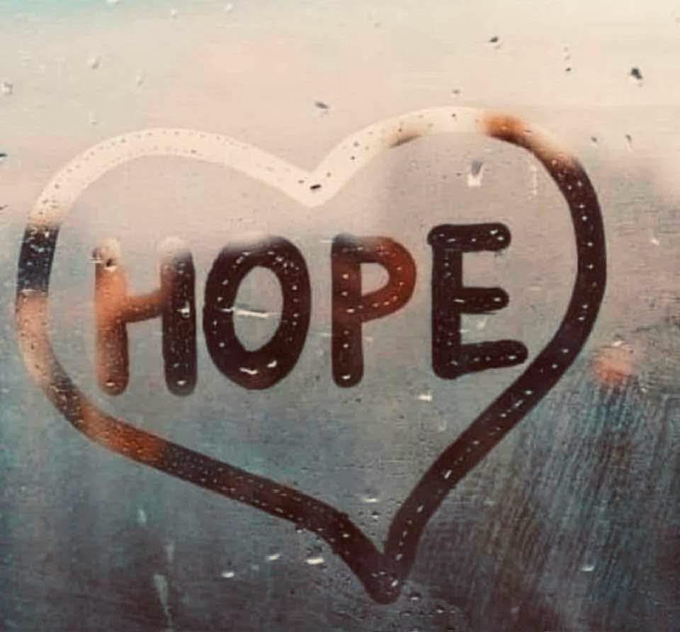 A heart drawn in the condensation on a foggy window with the word HOPE inside it, raindrops scattered on the glass